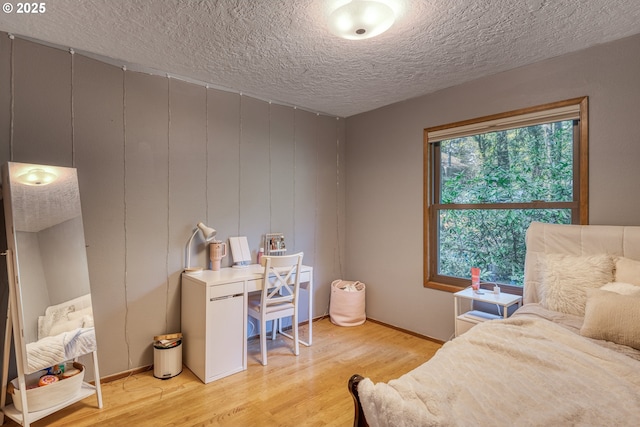 bedroom with baseboards, a textured ceiling, and light wood-style flooring