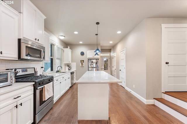 kitchen with pendant lighting, a kitchen island, white cabinets, and appliances with stainless steel finishes