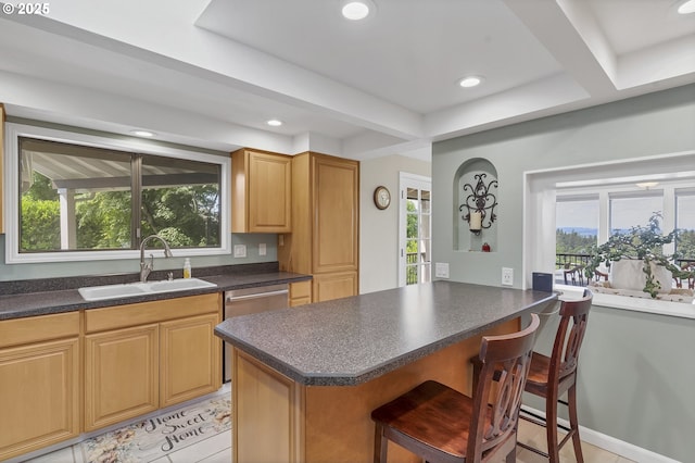 kitchen with a kitchen bar, dark countertops, dishwasher, and a sink