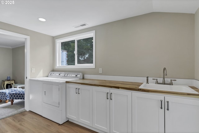 clothes washing area with visible vents, washing machine and dryer, light wood-style floors, cabinet space, and a sink