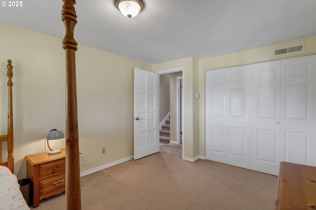 bedroom featuring baseboards, visible vents, a closet, a textured ceiling, and light carpet