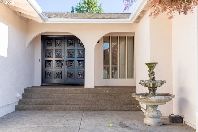 view of exterior entry featuring stucco siding and roof with shingles