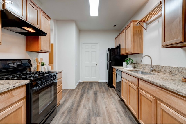 kitchen featuring wood finished floors, light stone countertops, under cabinet range hood, black appliances, and a sink