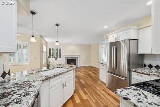 5364 Rosewood St, Lake Oswego, OR 97035 - kitchen with a sink, freestanding refrigerator, a lit fireplace, white cabinetry, and light wood-style flooring