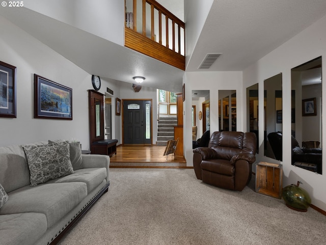 carpeted living room with visible vents, a towering ceiling, and stairway