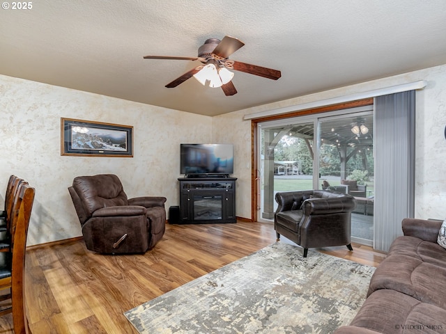 living area with ceiling fan, wood finished floors, baseboards, and a textured ceiling