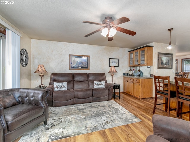 living area with ceiling fan, light wood-type flooring, and a textured ceiling