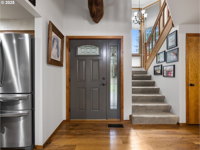 entryway featuring baseboards, a notable chandelier, wood finished floors, and stairs