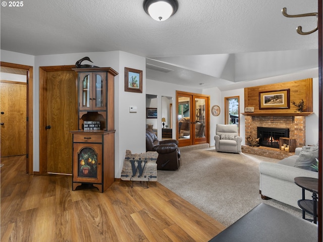 living room featuring lofted ceiling, a fireplace, french doors, wood finished floors, and a textured ceiling