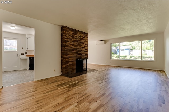 2220 Hayes St, Eugene, OR 97405 - unfurnished living room with an AC wall unit, light wood-type flooring, a fireplace, baseboards, and a textured ceiling