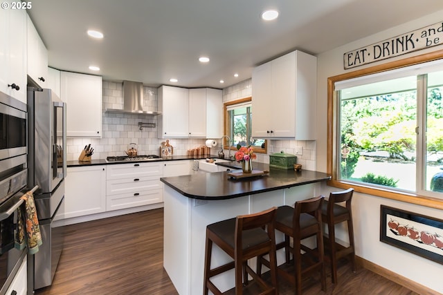 5339 SE Chase Rd, Gresham, OR 97080 - kitchen featuring wall chimney exhaust hood, appliances with stainless steel finishes, a peninsula, dark countertops, and recessed lighting