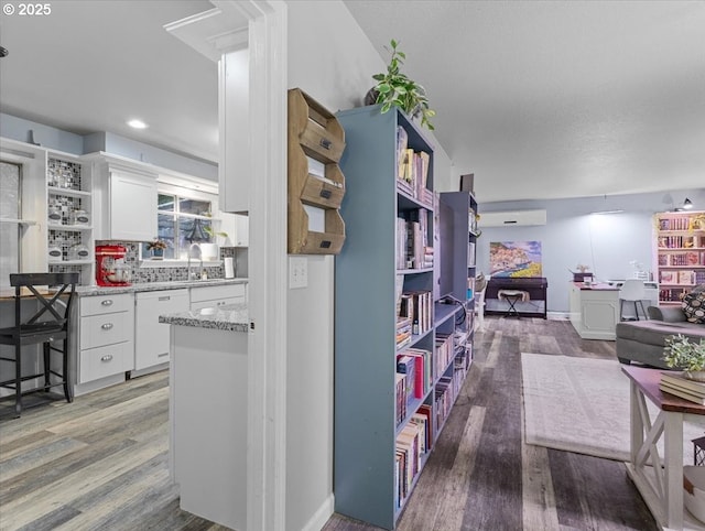 kitchen with hardwood / wood-style flooring, a wall unit AC, white dishwasher, light stone counters, and white cabinets