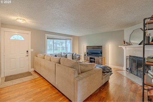 living room with a tiled fireplace, a textured ceiling, baseboards, and light wood-type flooring