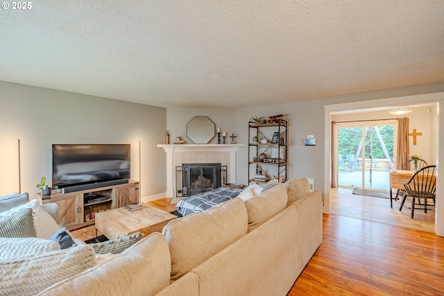 living area featuring a tiled fireplace, light wood finished floors, and a textured ceiling