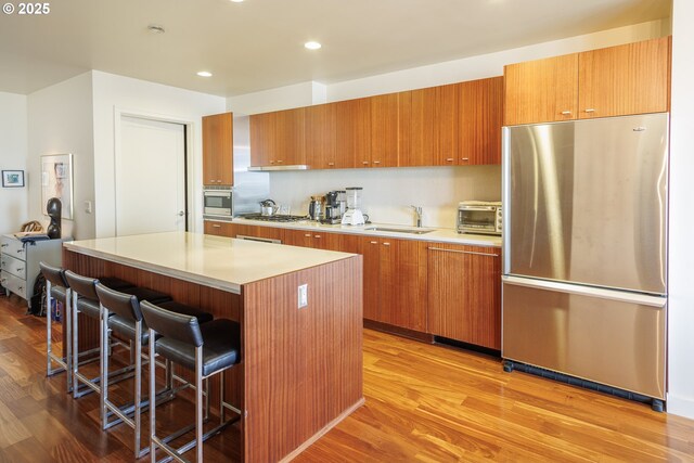 kitchen featuring appliances with stainless steel finishes, brown cabinetry, light wood-type flooring, a center island, and recessed lighting
