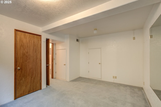 unfurnished room with a textured ceiling, light colored carpet, and visible vents