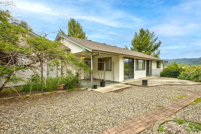 back of property featuring fence, a shingled roof, a mountain view, and a patio area