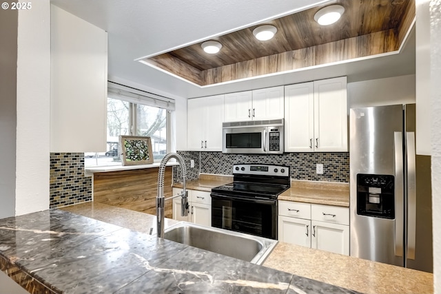 kitchen with appliances with stainless steel finishes, tasteful backsplash, white cabinetry, a tray ceiling, and wooden ceiling