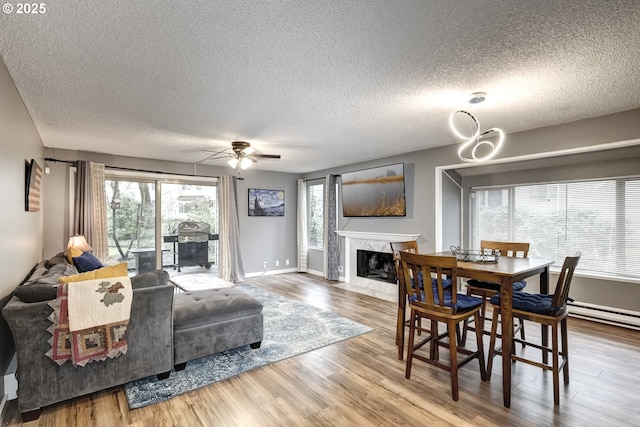 dining space with a premium fireplace, hardwood / wood-style floors, a textured ceiling, and ceiling fan