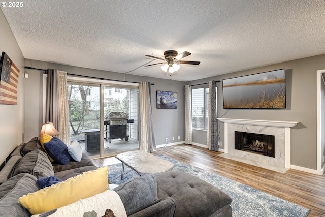 living room with ceiling fan, a high end fireplace, hardwood / wood-style floors, and a textured ceiling