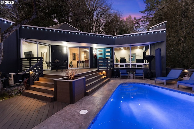 pool at dusk with a wooden deck and a patio area