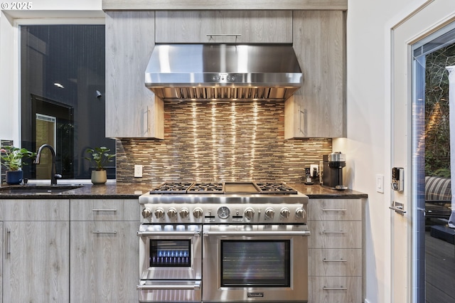 kitchen featuring modern cabinets, a sink, double oven range, tasteful backsplash, and wall chimney exhaust hood