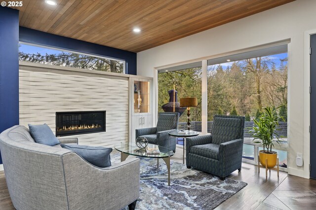 living room with a glass covered fireplace, plenty of natural light, wooden ceiling, and recessed lighting