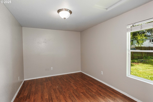 unfurnished room with dark wood-type flooring, attic access, and baseboards