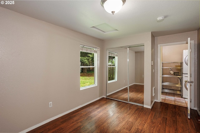 unfurnished bedroom with stacked washing machine and dryer, attic access, wood finished floors, a closet, and baseboards