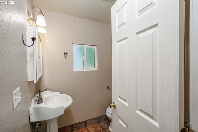 bathroom with toilet, stone finish flooring, and a sink