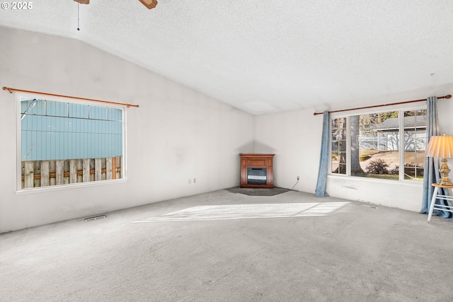 unfurnished living room with lofted ceiling, ceiling fan, carpet floors, and a textured ceiling