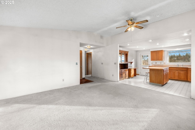 unfurnished living room with lofted ceiling, sink, light colored carpet, ceiling fan, and a textured ceiling