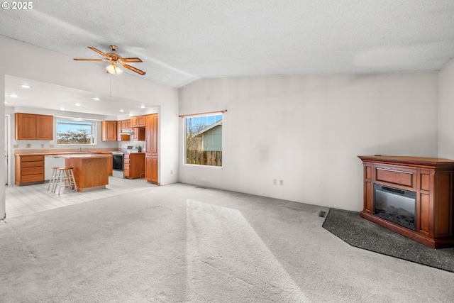 unfurnished living room with vaulted ceiling, light carpet, ceiling fan, and a textured ceiling