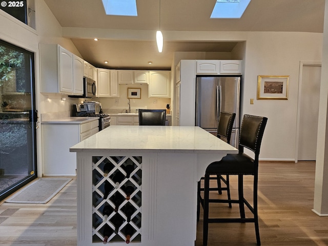 kitchen featuring a skylight, hanging light fixtures, stainless steel appliances, a kitchen island, and white cabinets