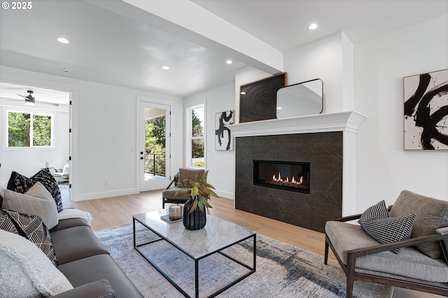 living room with baseboards, ceiling fan, light wood-type flooring, recessed lighting, and a premium fireplace