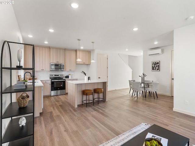 kitchen featuring light wood finished floors, a wall unit AC, stainless steel appliances, light brown cabinetry, and backsplash