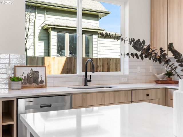 kitchen with light countertops, light brown cabinets, dishwasher, and a sink