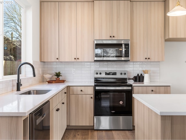 kitchen with light brown cabinets, stainless steel appliances, wood finished floors, a sink, and tasteful backsplash