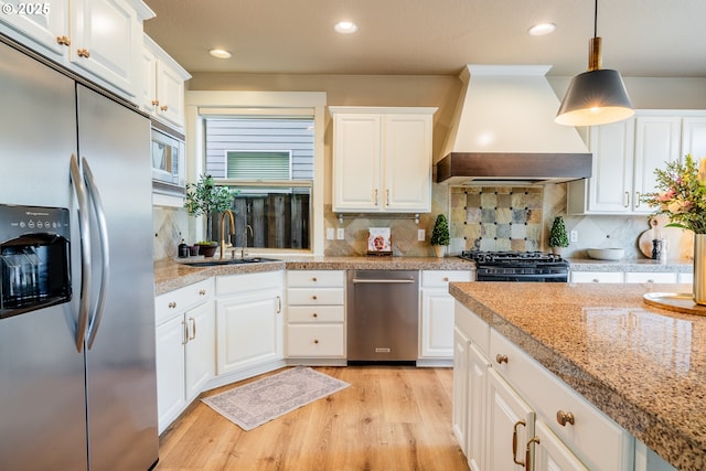 kitchen featuring sink, custom exhaust hood, white cabinetry, decorative light fixtures, and stainless steel appliances