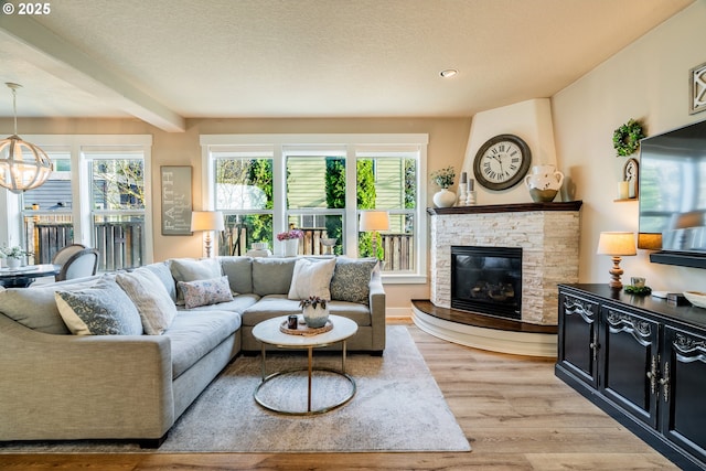 living room with light hardwood / wood-style flooring, beam ceiling, a textured ceiling, a stone fireplace, and a chandelier