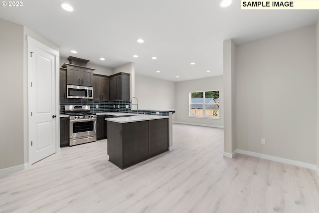 kitchen featuring appliances with stainless steel finishes, open floor plan, a peninsula, light countertops, and backsplash