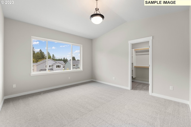 unfurnished bedroom with carpet, a walk in closet, lofted ceiling, a closet, and baseboards