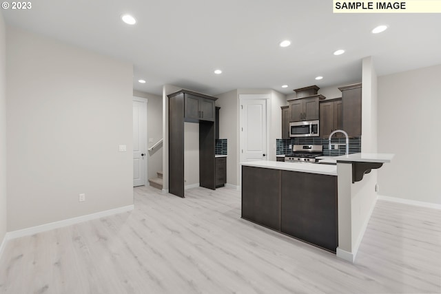 kitchen with stainless steel appliances, tasteful backsplash, a sink, dark brown cabinets, and a peninsula