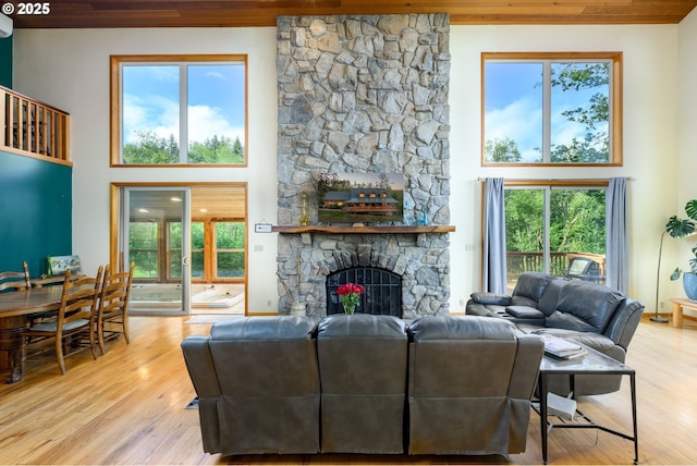 living room featuring a high ceiling, a stone fireplace, and light hardwood / wood-style flooring