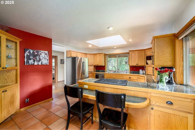 kitchen featuring sink, a skylight, appliances with stainless steel finishes, a kitchen breakfast bar, and kitchen peninsula