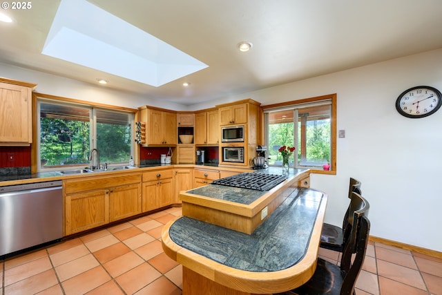 kitchen featuring sink, a skylight, stainless steel appliances, light tile patterned flooring, and tile countertops