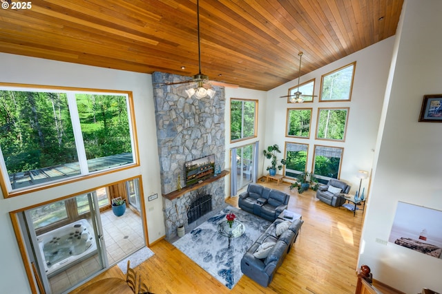 living room with a stone fireplace, wood ceiling, wood-type flooring, high vaulted ceiling, and ceiling fan