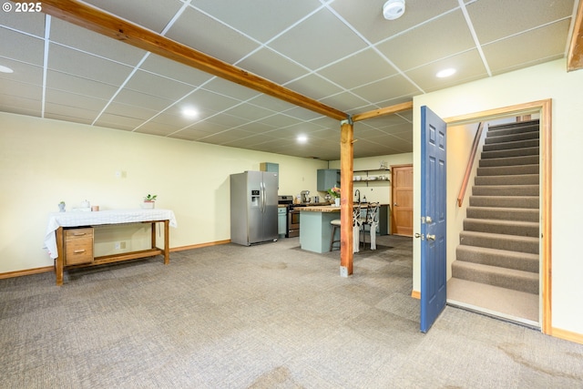 basement featuring a paneled ceiling, stainless steel fridge, and light carpet