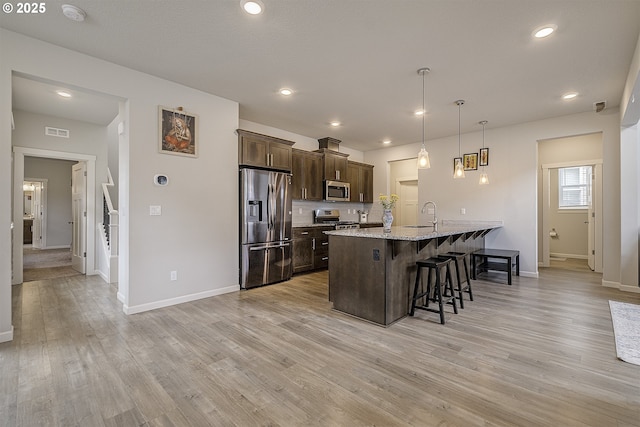 30942 NW Turel Dr, North Plains, OR 97133 - kitchen featuring stainless steel appliances, a kitchen bar, dark brown cabinets, baseboards, and light wood-type flooring