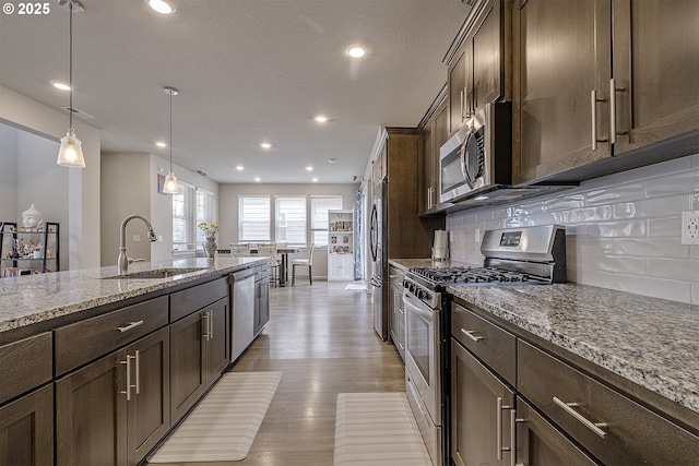 30942 NW Turel Dr, North Plains, OR 97133 - kitchen featuring appliances with stainless steel finishes, a sink, dark brown cabinetry, light stone counters, and light wood-style floors